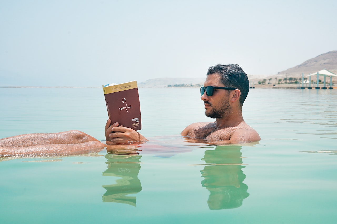 A Man Wearing Sunglasses Is Reading A Book In The Ocean