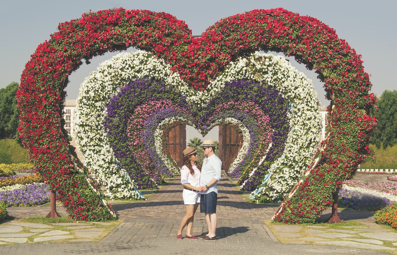 A couple wearing matching polo shirts under the heart-shaped flower arcs