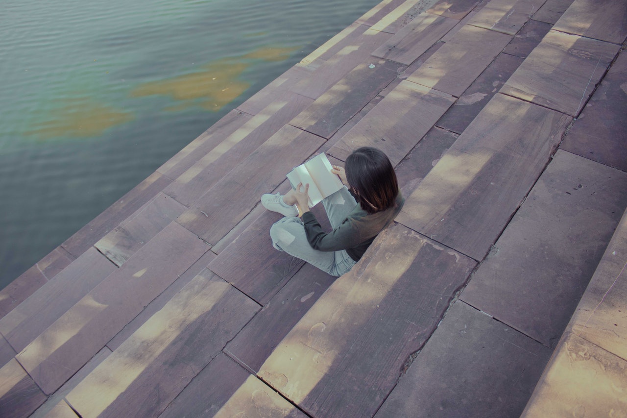 Woman Reading a Book Near a Body of Water