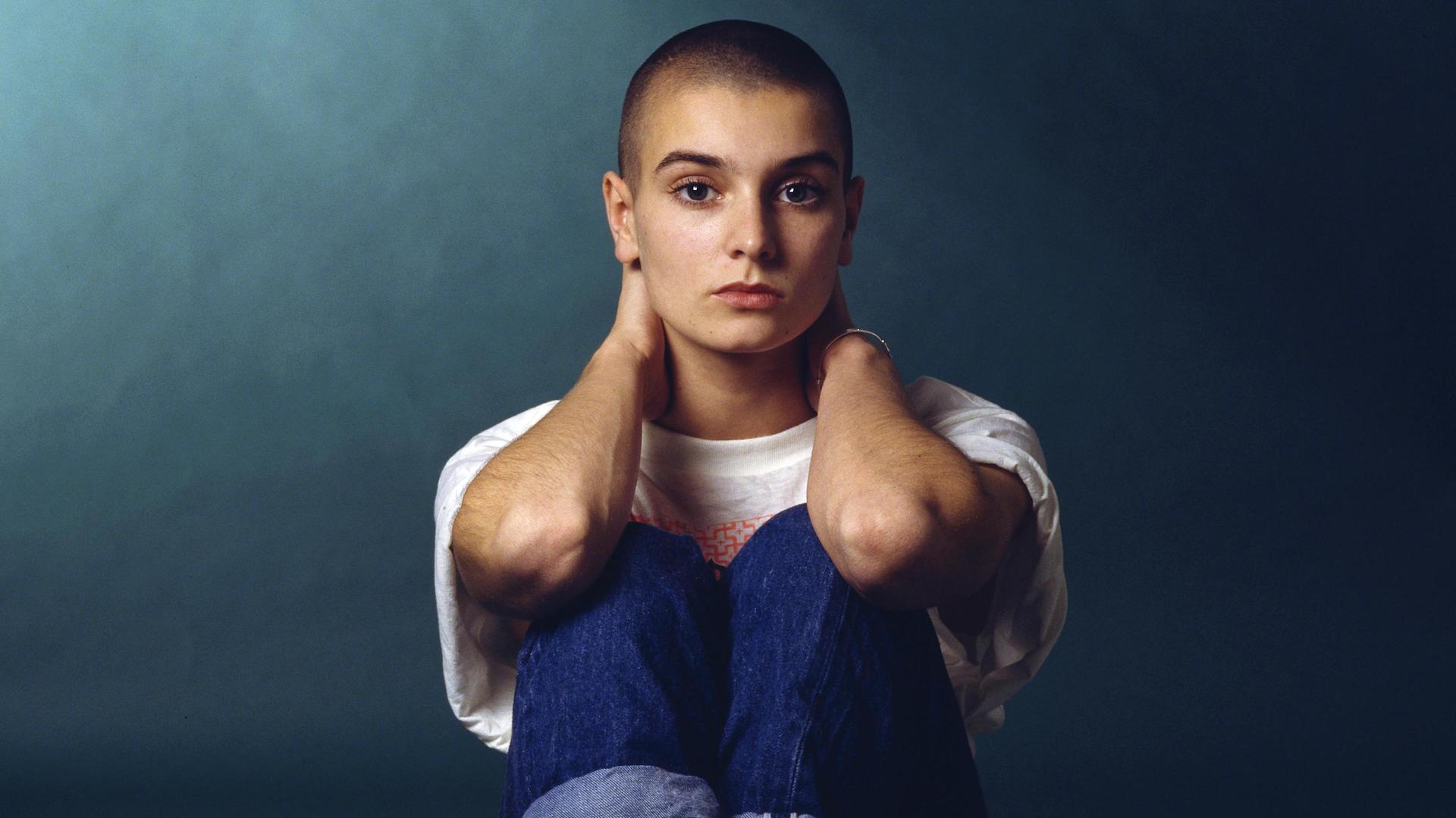 Sinéad O'Connor sitting with her hands on her neck