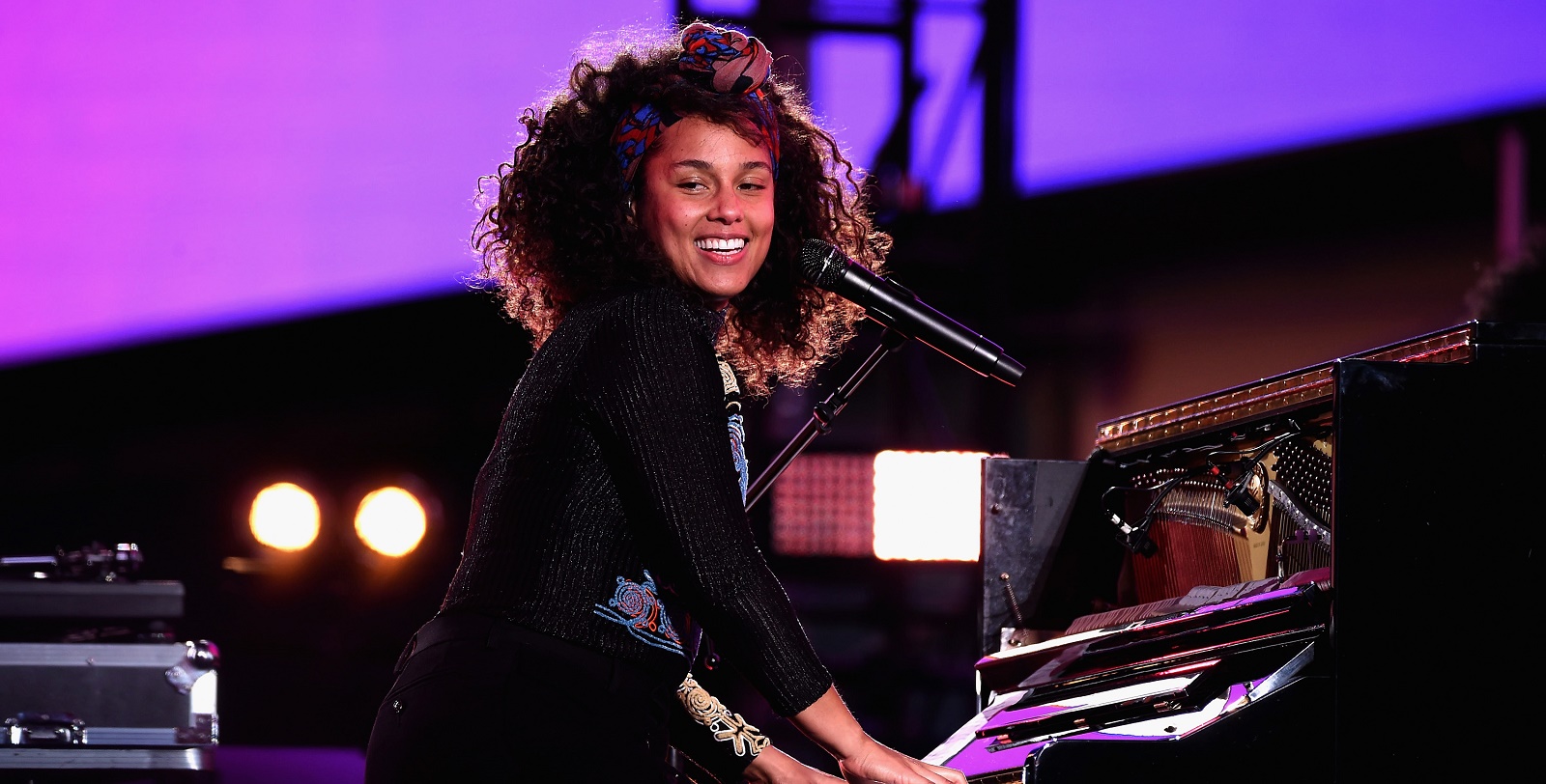 Alicia keys smiling and playing piano while on the stage