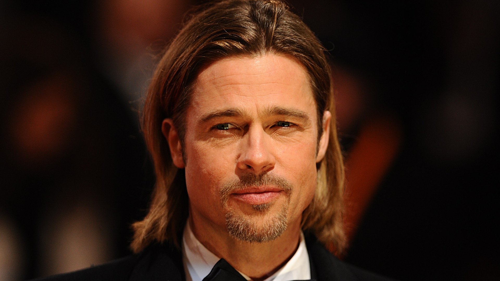 Brad Pitt with long blonde hair wearing a balck suit 