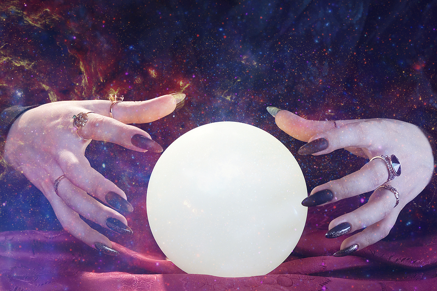 A witch with long nails and wearing multiple rings doing psychic reading on a magic ball