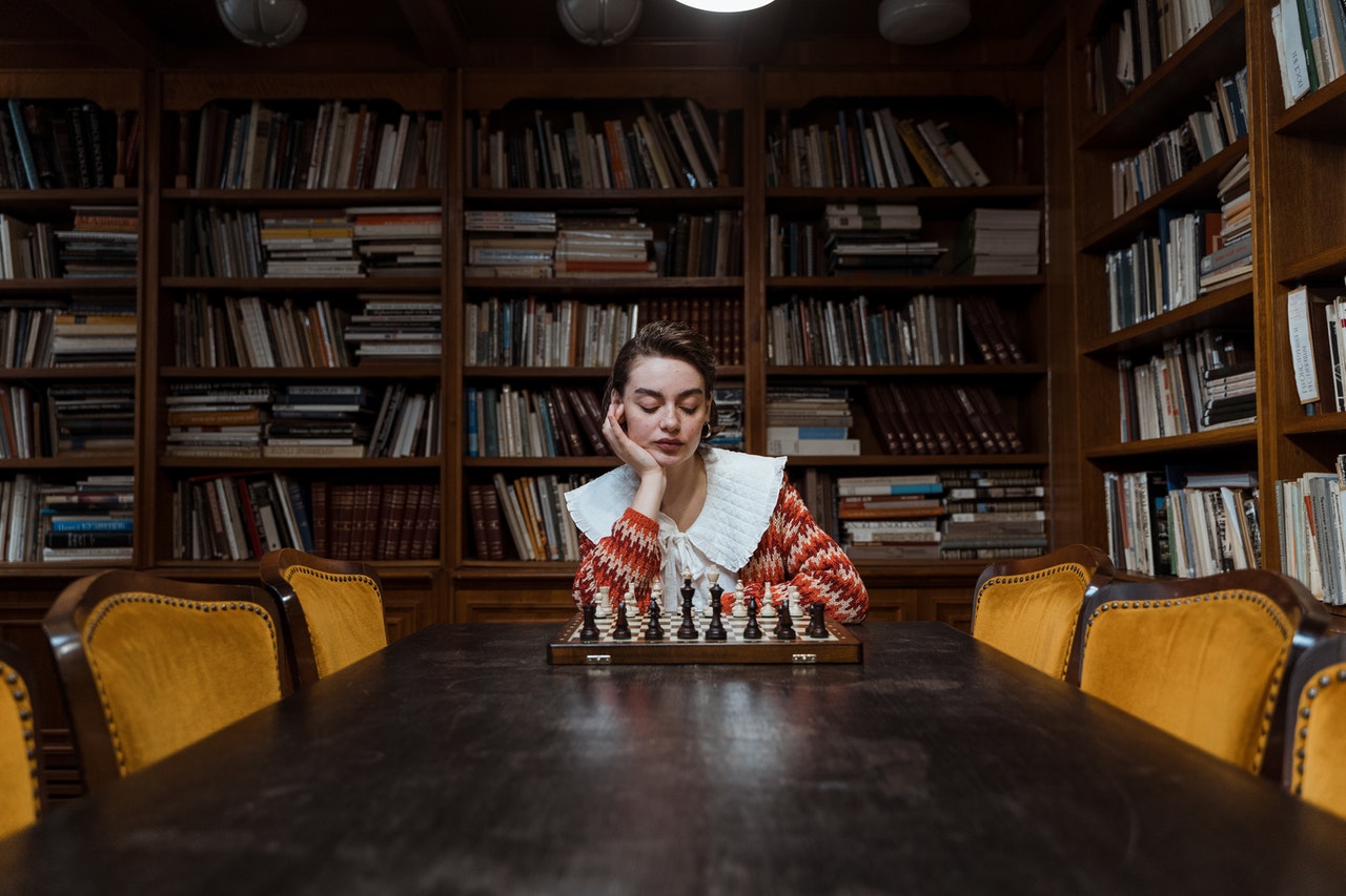 Pensive Woman playing Chess inside a library