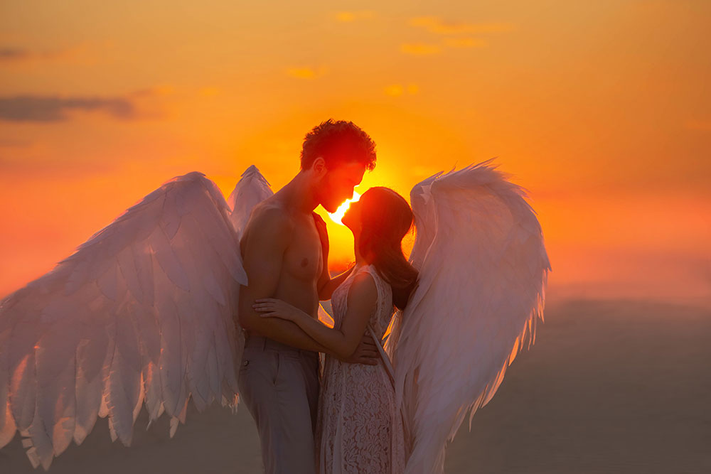 A man and woman angels holding each other in front of the sunset