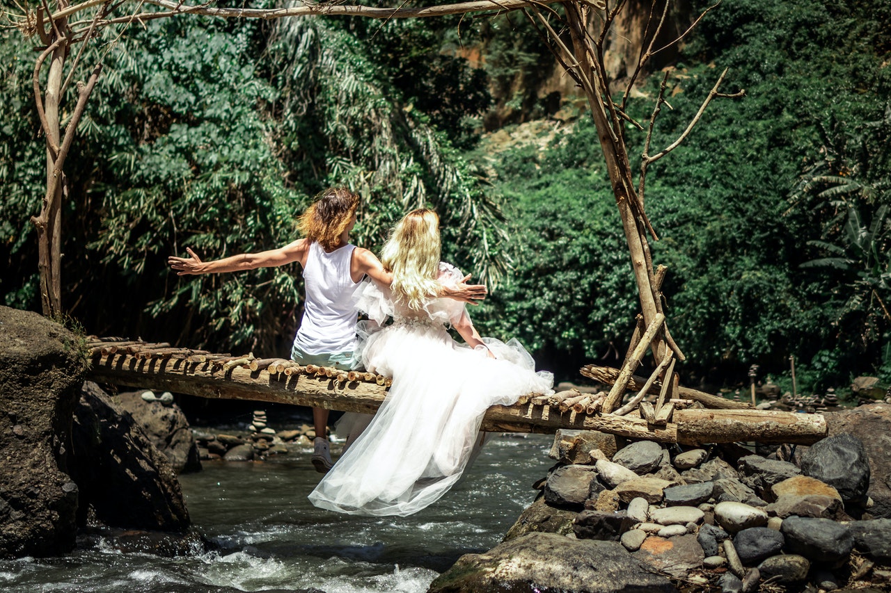 Groom And Bride sitting on a log above a river with the man's arms stretched out