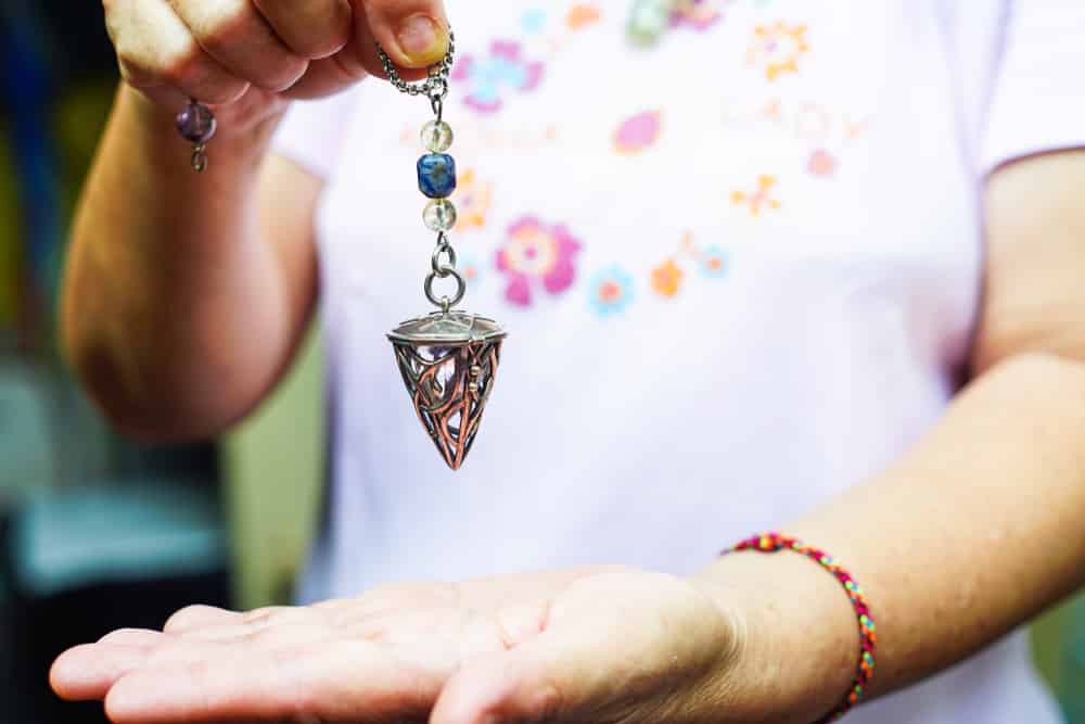 A woman holding a steel pendulum with beads