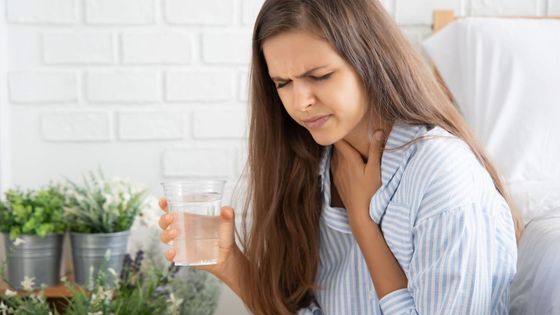 Woman Drinking Water and holding her neck with grimace on her face