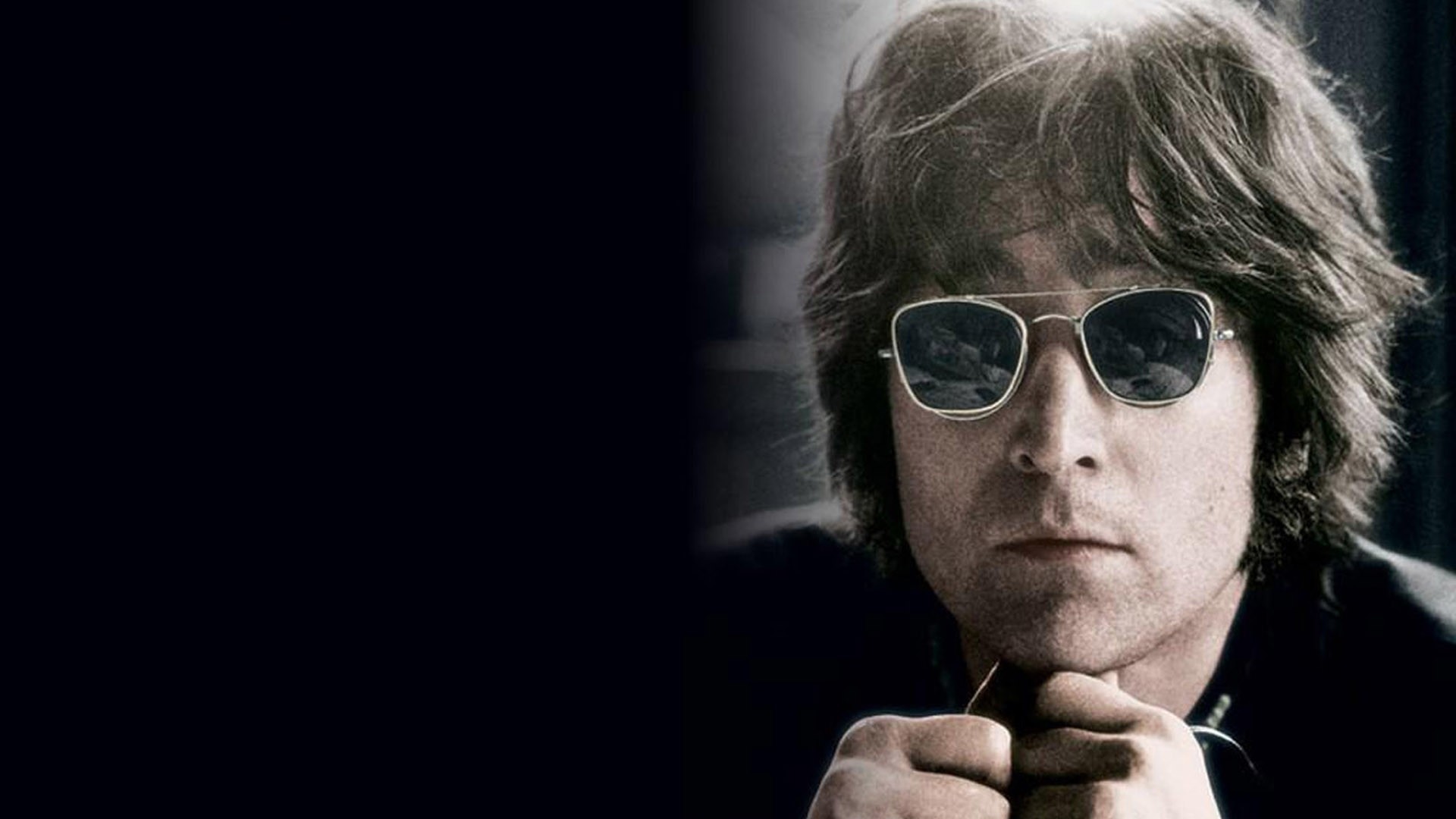 John Lennon wearing sunglasses with his hands on his chin