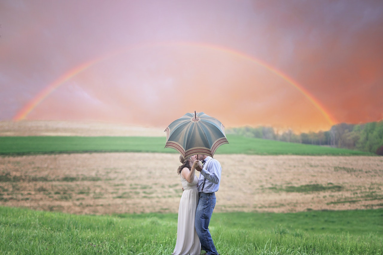 Couple Holding Umbrella While Kissing with a rainbow at the background