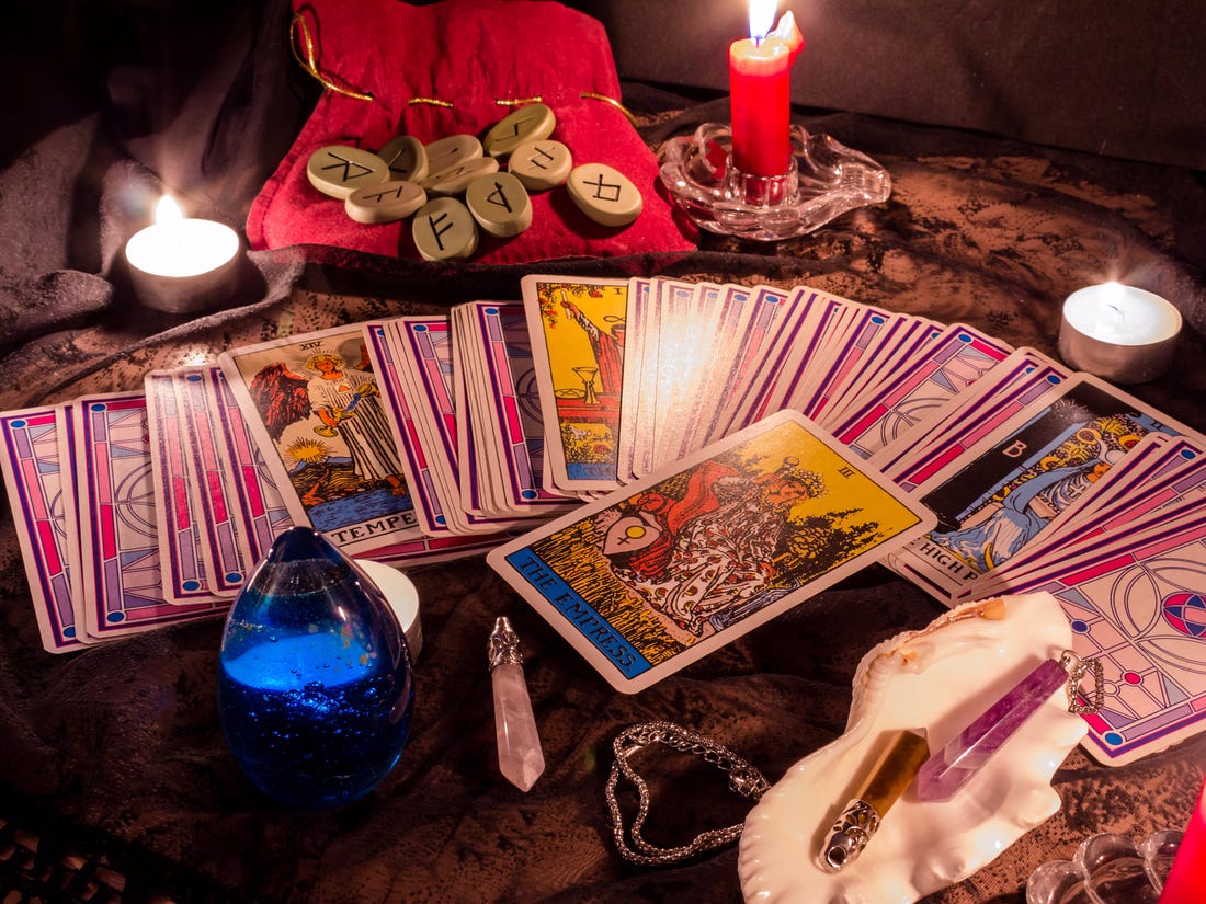 Different tarot cards, pendulum, candles and other psychic ornaments placed on a table