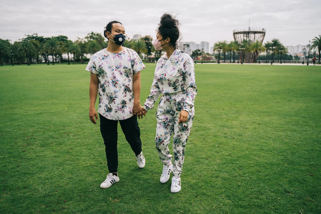 Couple with Face Masks Standing on Green Grass Field While Holding Hands
