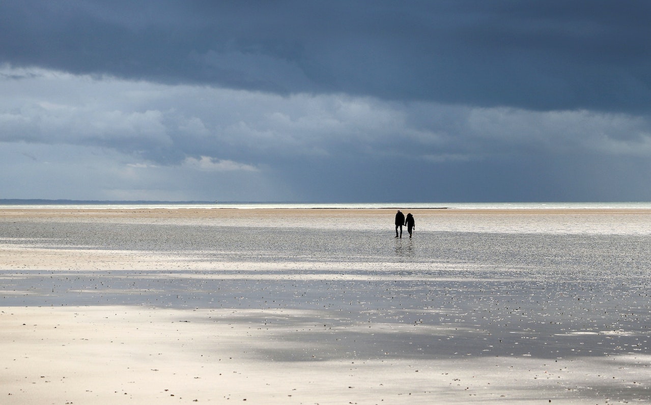 Couple Walking on Beach under Clouds