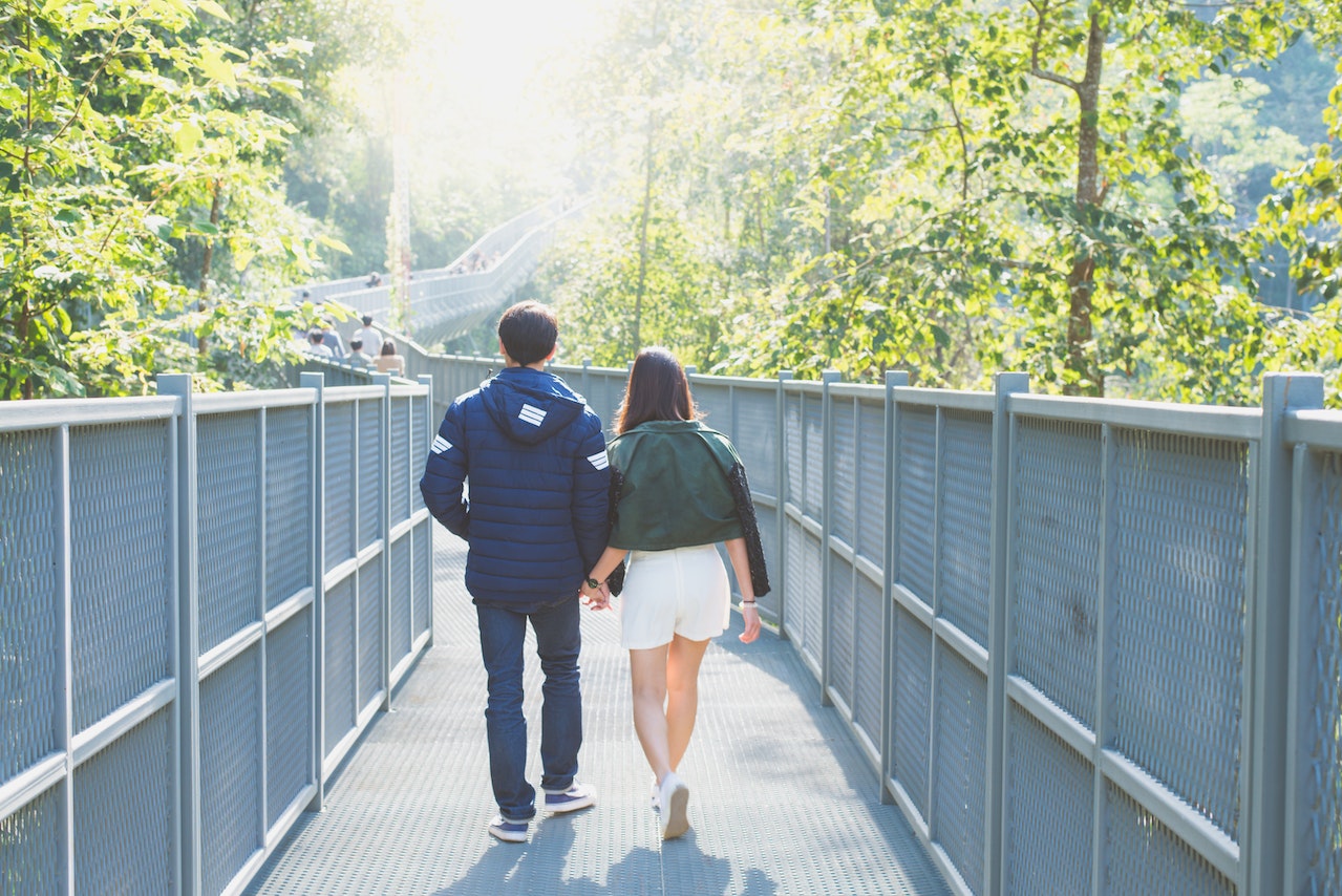 Man and Woman Holdings Hands While Walking on Bridge