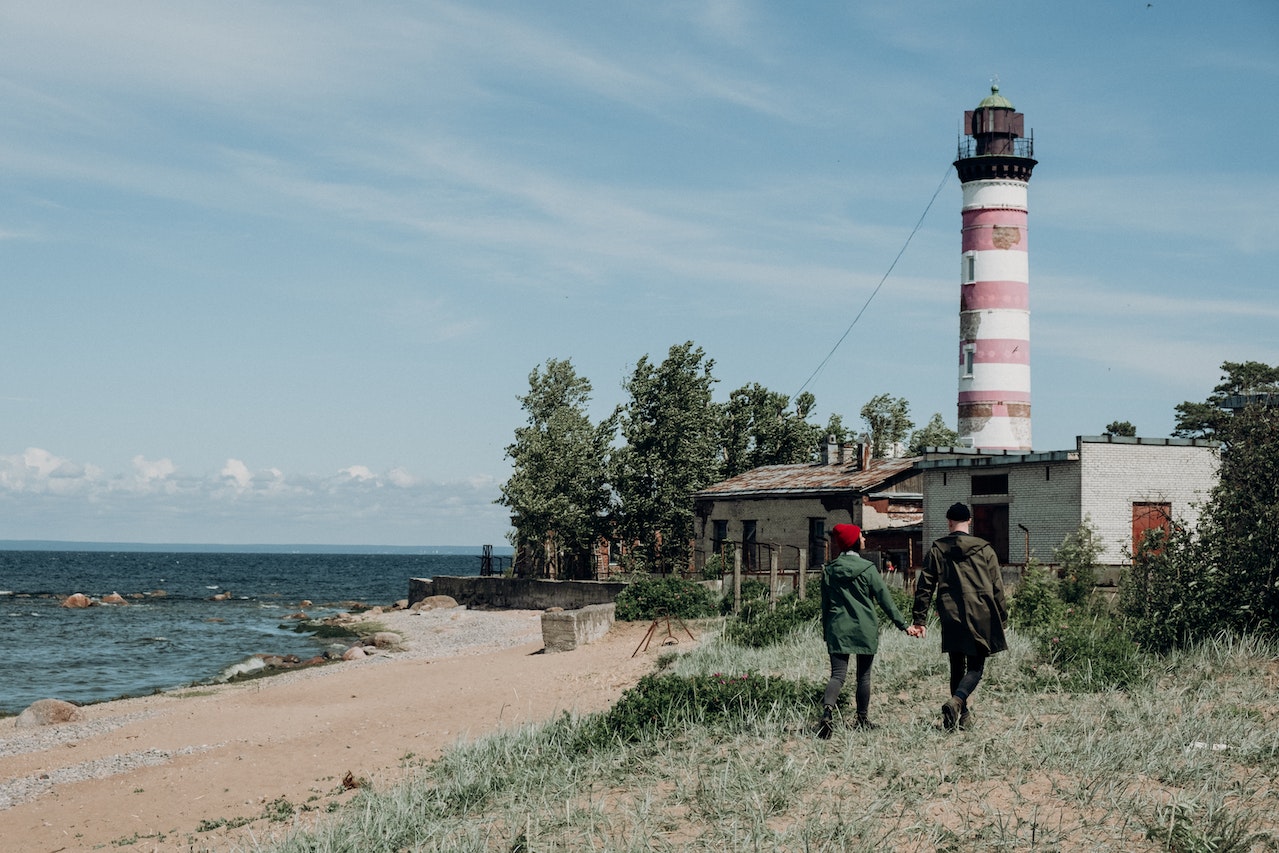 Couple Holding Hands While Walking Near a Lighthouse