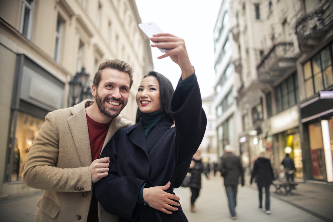 Woman In Black Coat Taking Selfie with Guy in brown coat