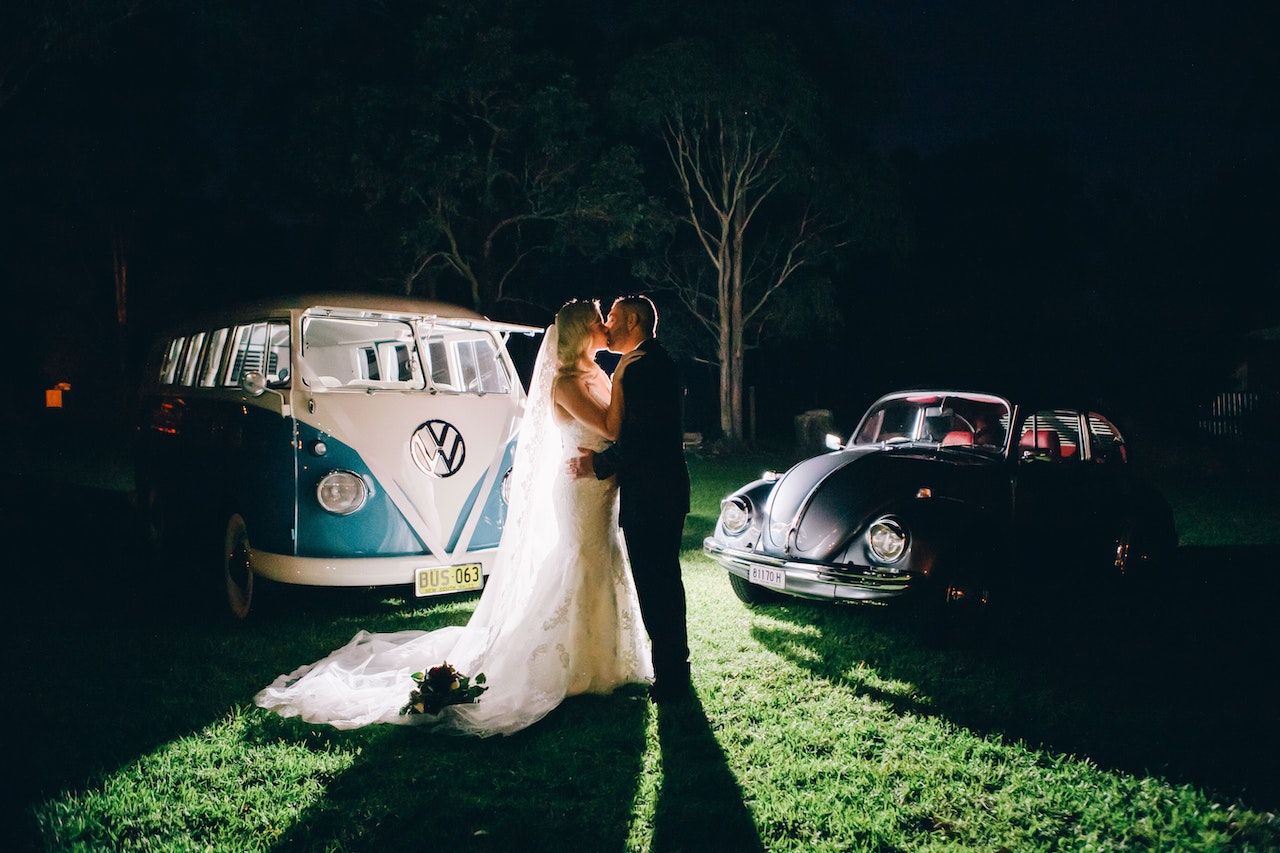 A Bride And Groom kissing in the middle of two cars