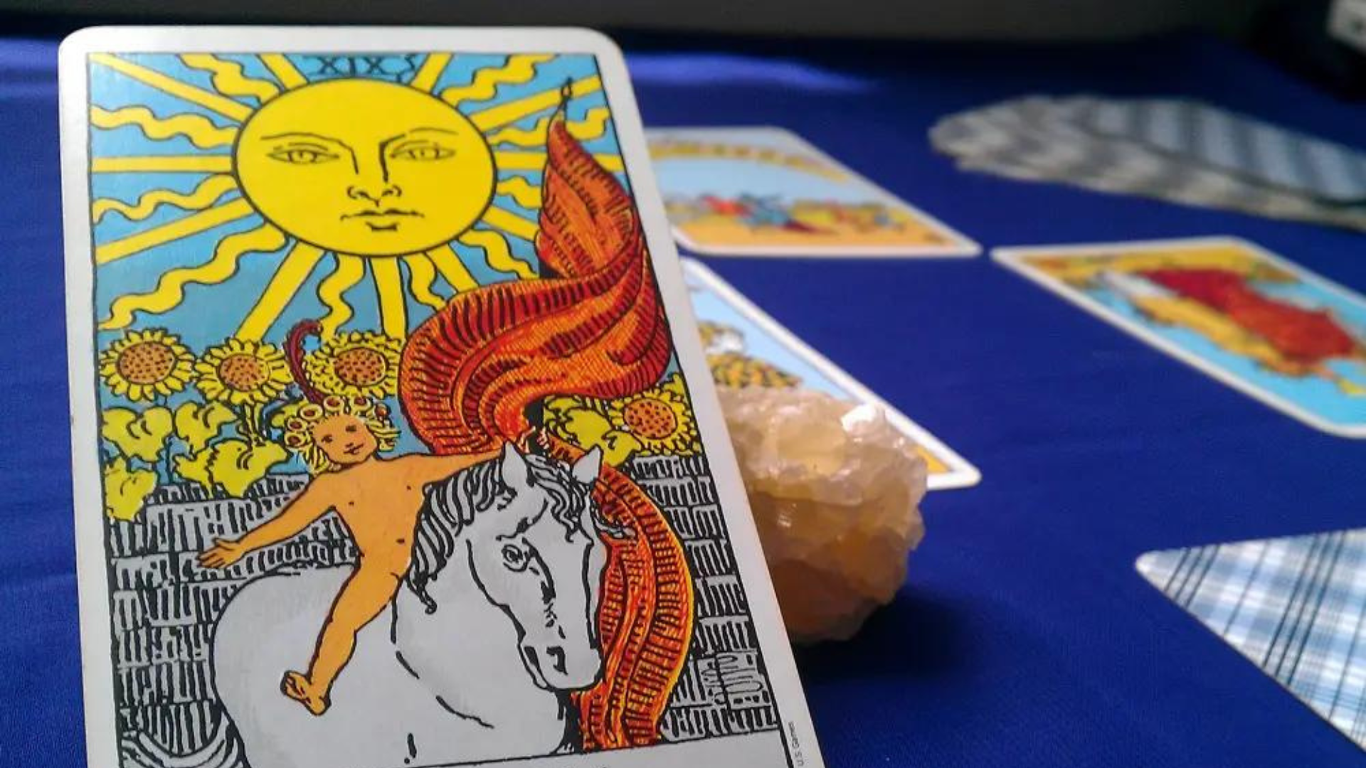 The Sun tarot card leaning on a crystal stone on top of a blue table