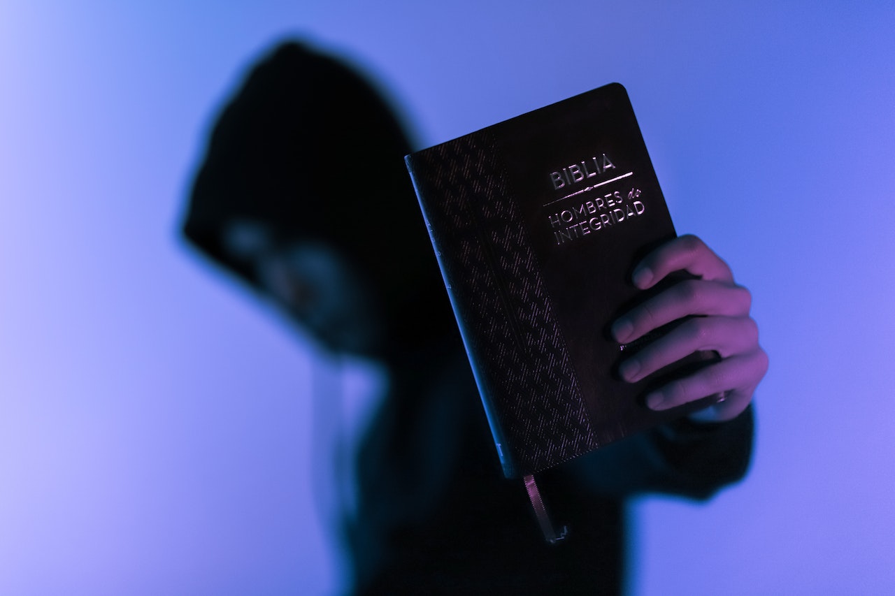 Person Wearing A Hoodie Holding The Bible Forward