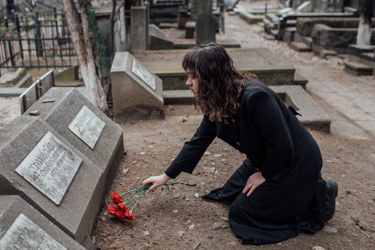 A Woman in Black Dress Offering Flowers on a Tombstone