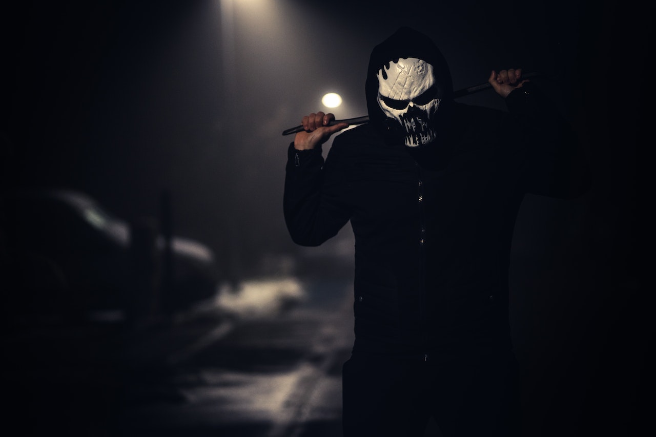 Person in Black Jacket Wearing White Scary Mask and carrying a stick