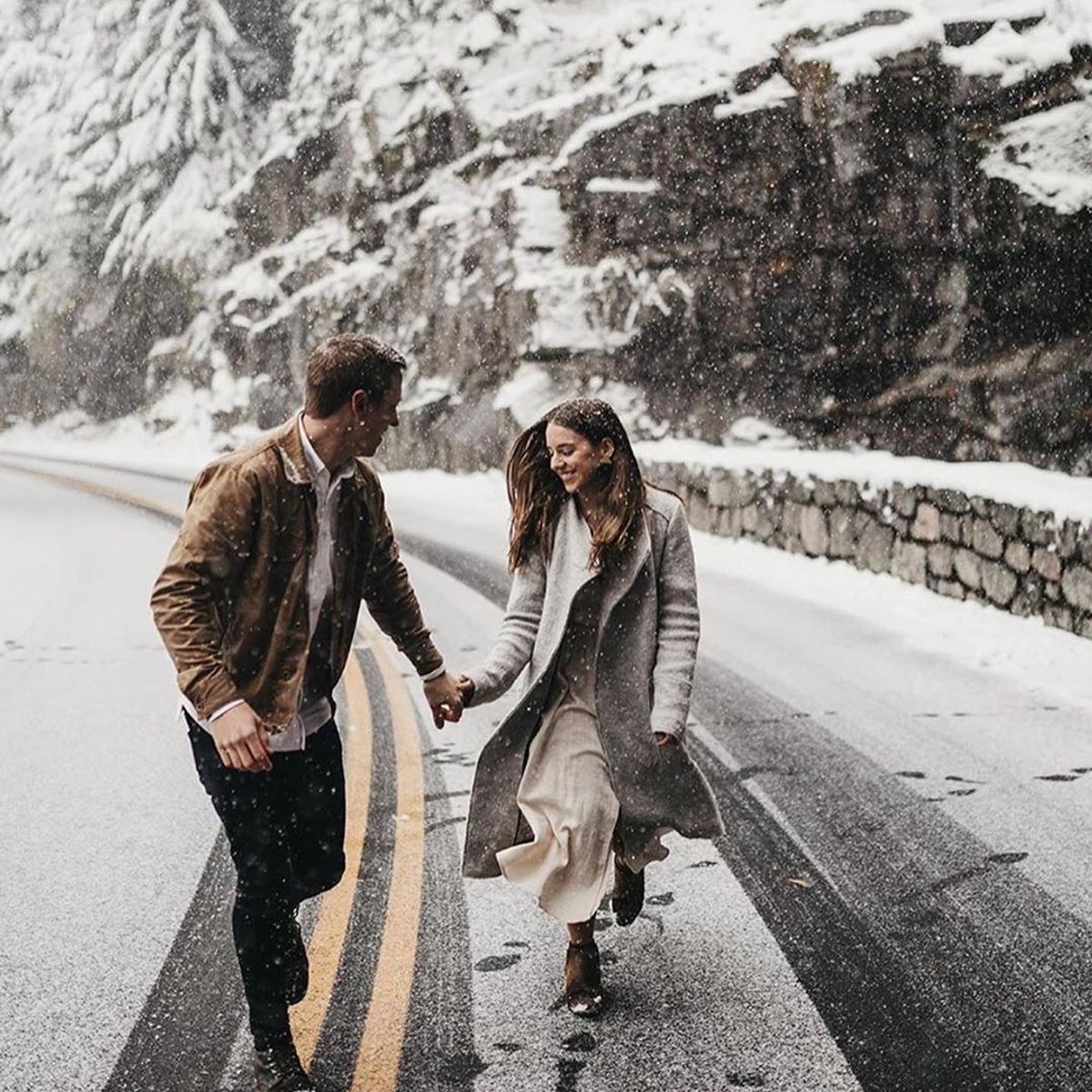 A couple holding hands, happily walking on the road while it's snowing