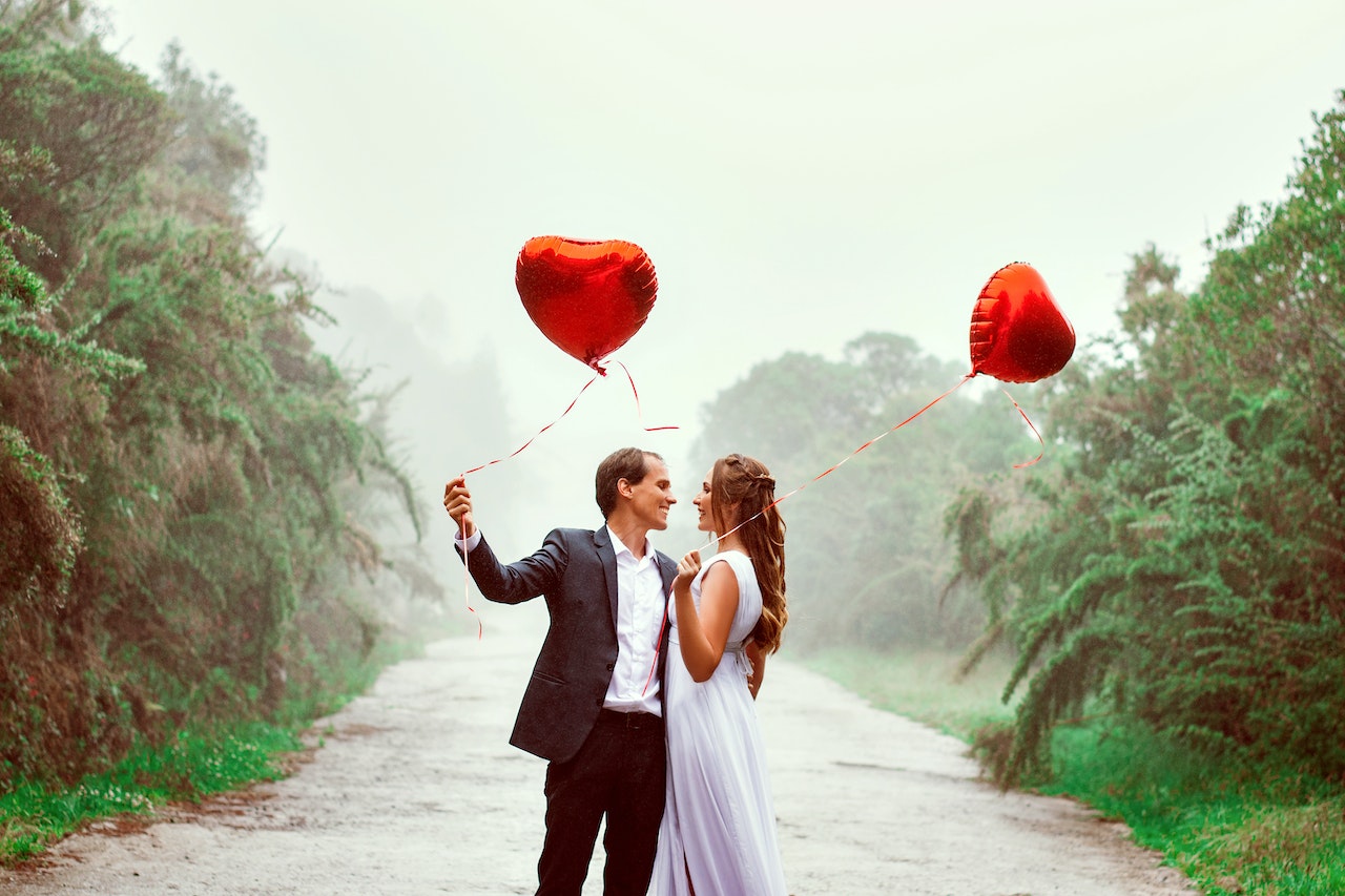 Man and woman each holding a red hear balloon looking at each other