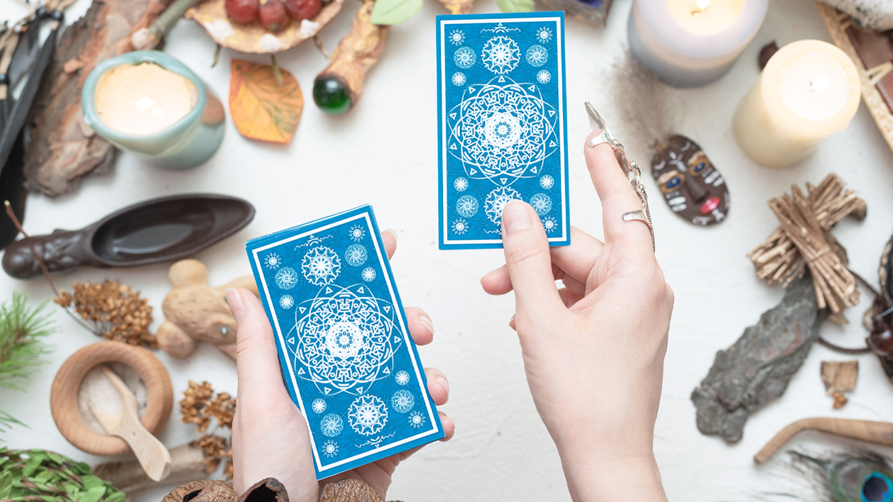 A person holding blue tarot cards with some psyhcic stones and ornaments around her