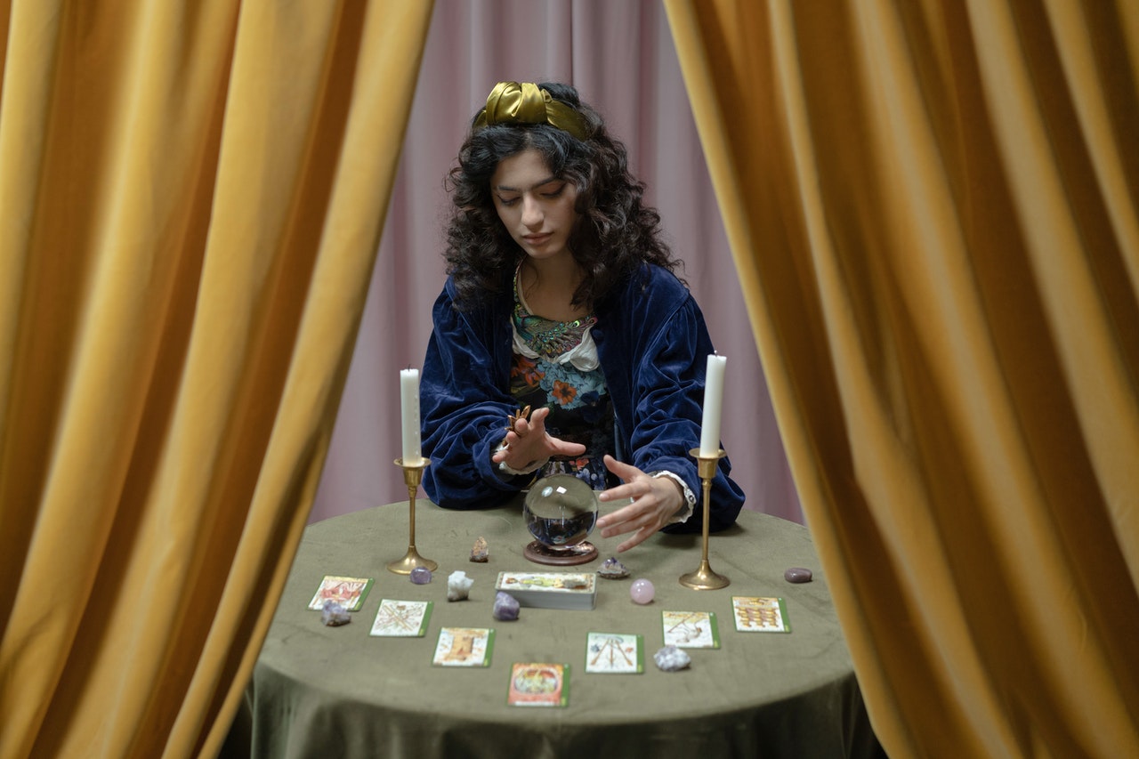A Woman Fortune Telling With Tarot Cards, Candles, And Crystal Ball On The Table