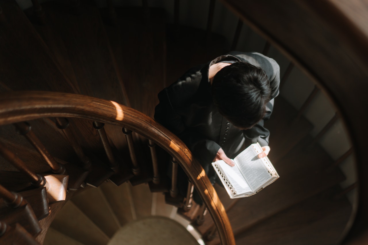 A Person Reading A Bible While Going Down The Stairs
