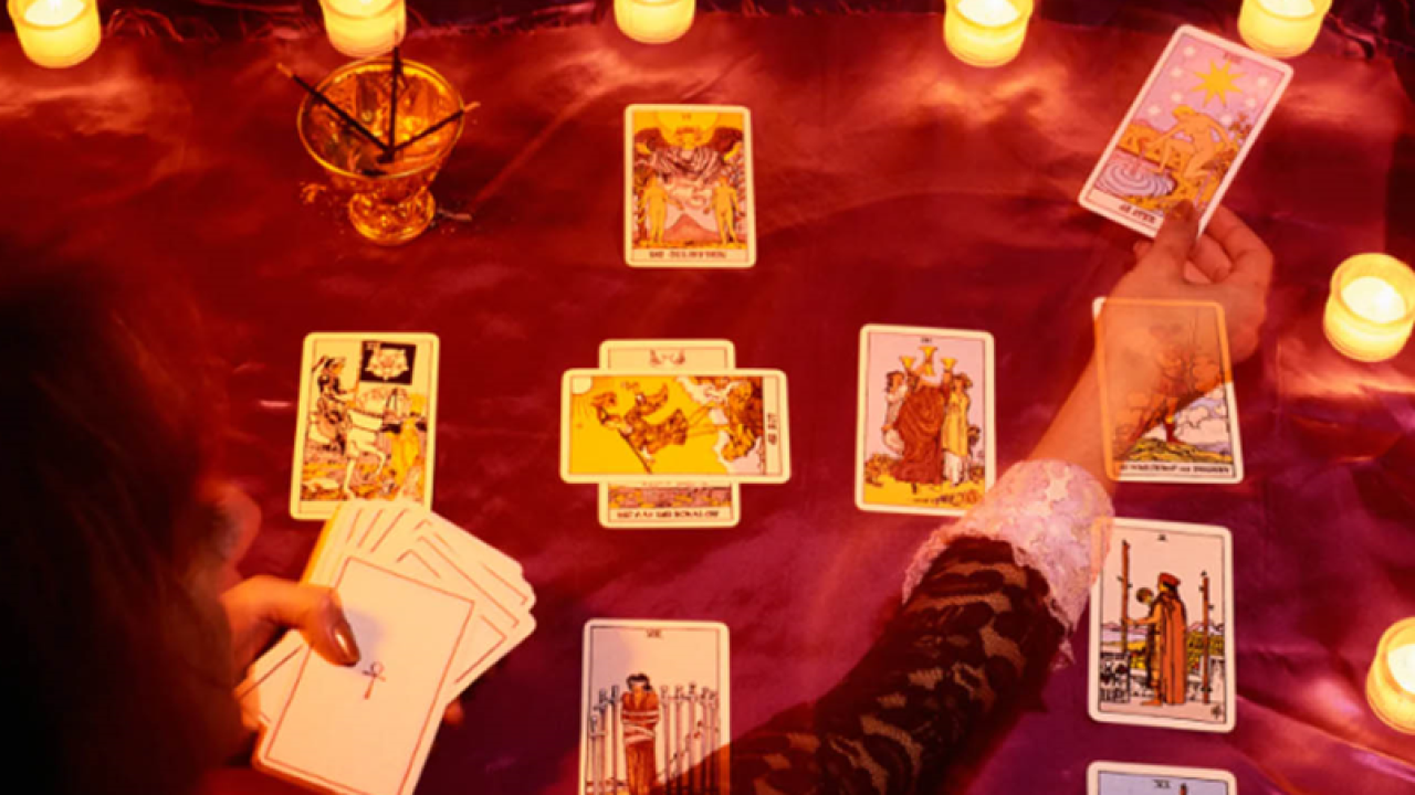 A psychic holding tarot cards while sitting on a table with candles