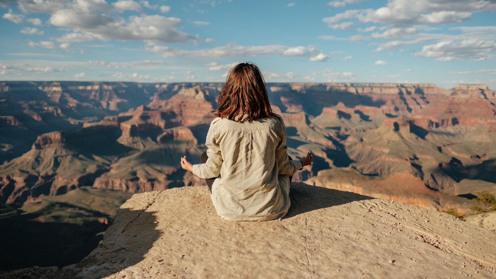 An adult woman in long sleeve polo on a meditation pose facing the Grand Canyon in Arizona, USA