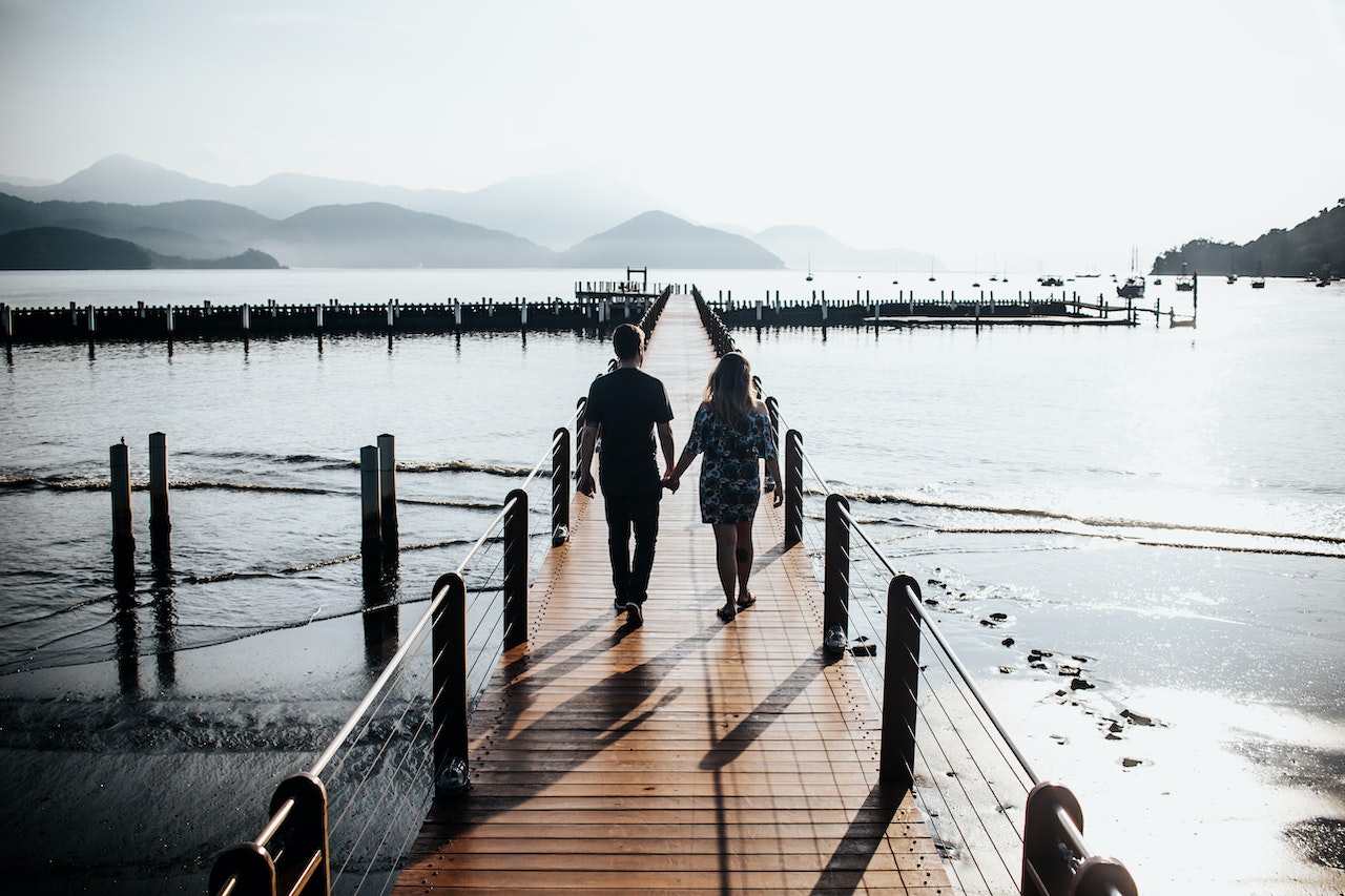 Couple Holding Hands While Walking Down Wooden Dock
