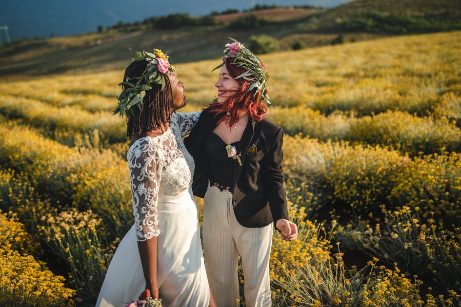 Two girls wearing a flower crown, one wearing a wedding dress and the other suit coat in a field