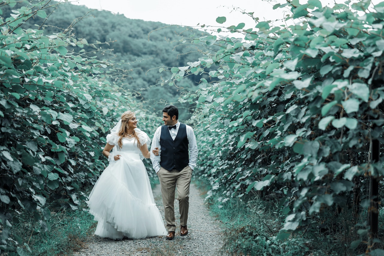 Bride and Groom Walking on a Pathway Between Plants