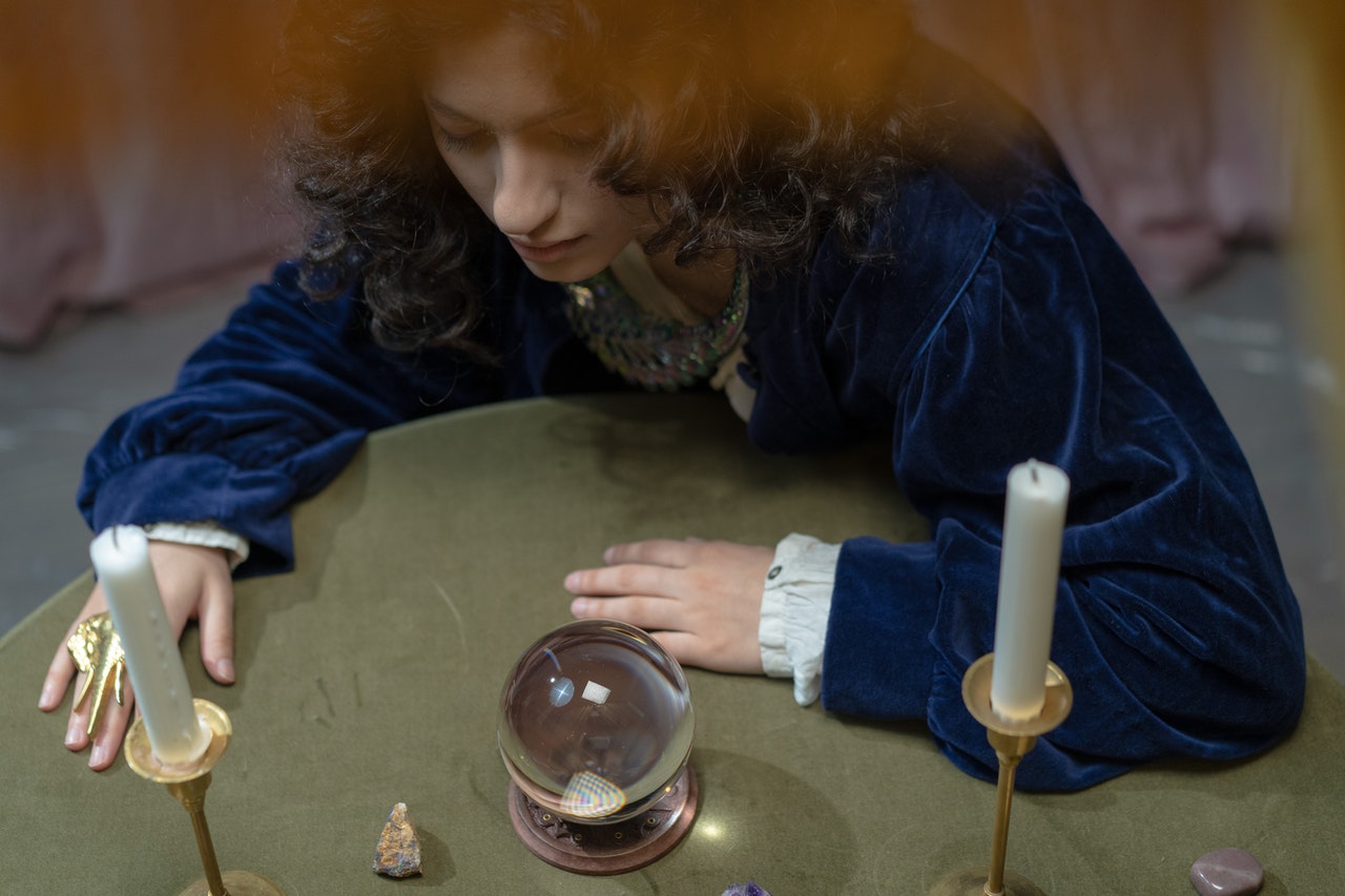 A Woman in Blue Velvet Top Looking at a Crystal Ball on a Table