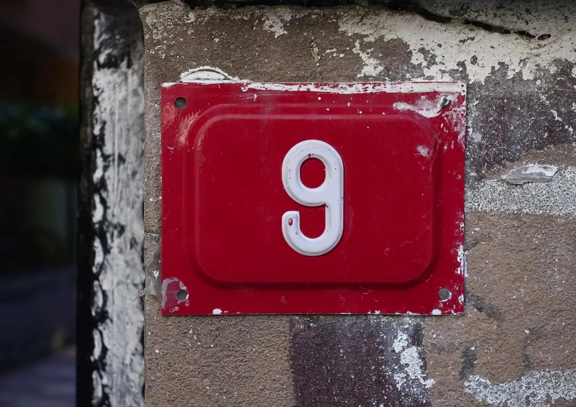 A brick wall having a red metal plate with number 9