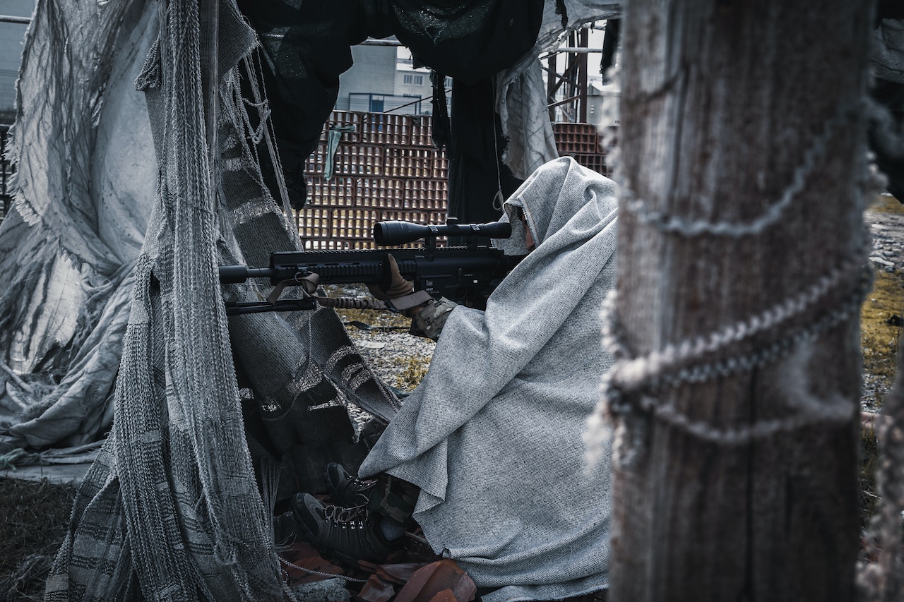 A soldier covered in grey blanket while aiming at someone