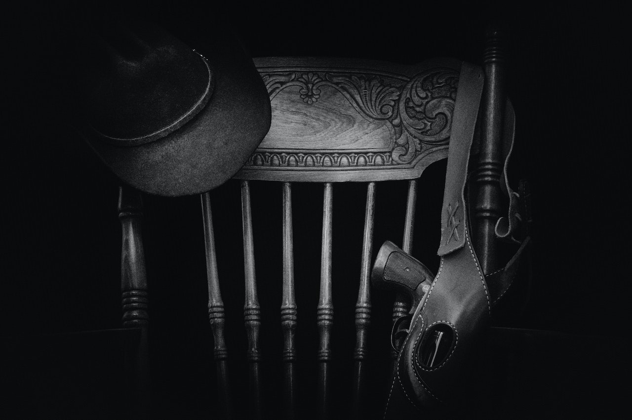 A gun on a gun sling bag and a black hat hanging on a vintage chair
