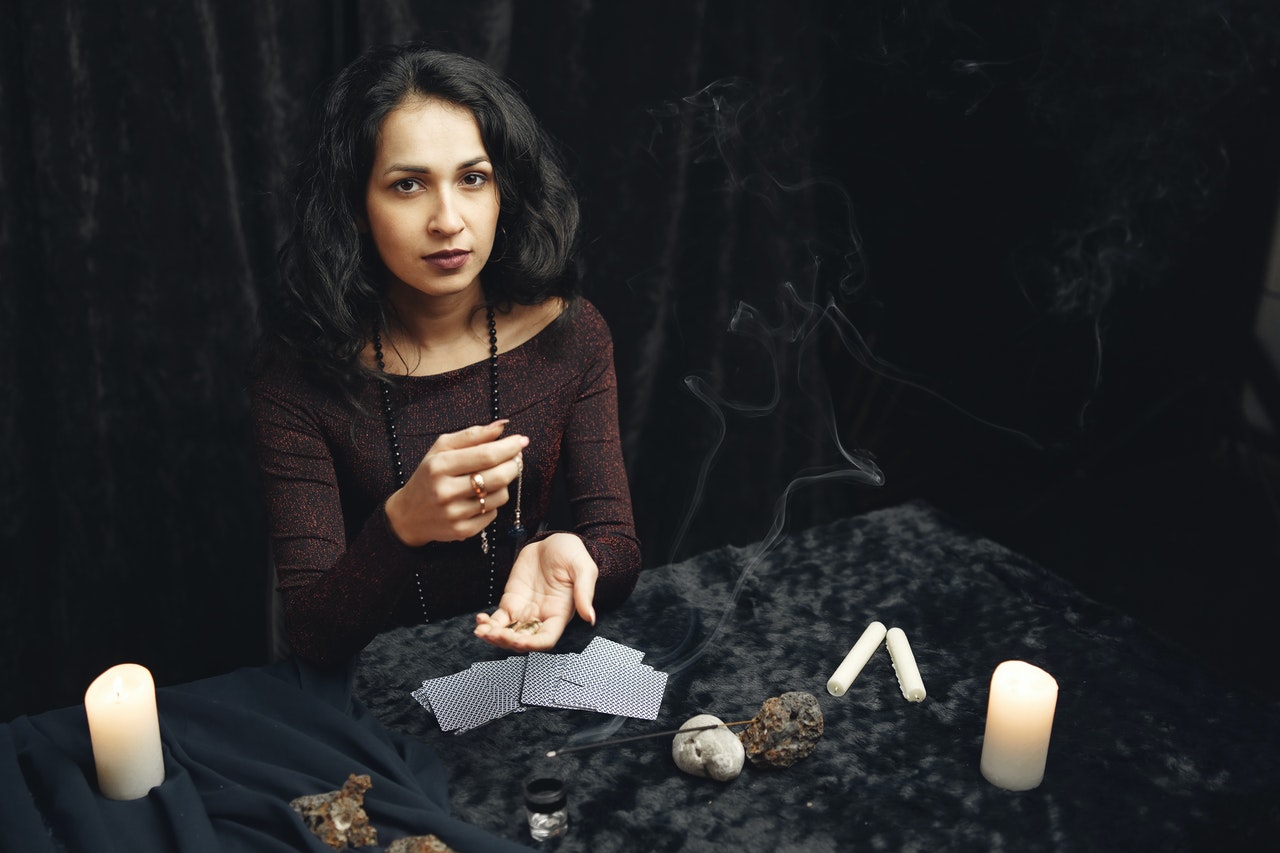 Woman in Black Long Sleeves Sitting At A Table with Tarot Cards And Candles