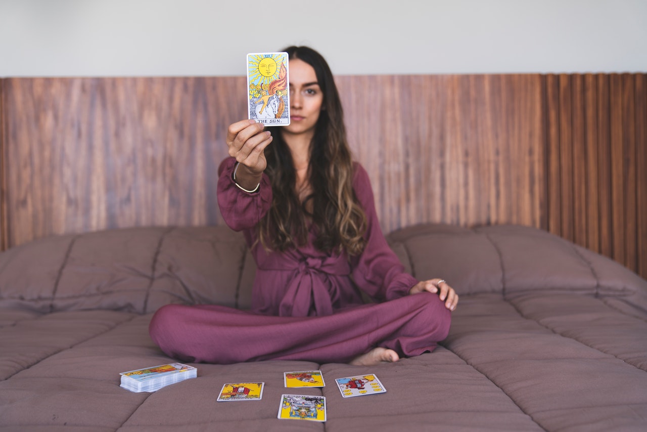 Curly Haired Female Holding a Tarot Card While Sitting On The Bed