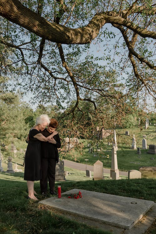 Elderly woman hugging young boy while in front of a tomb in the cemetery