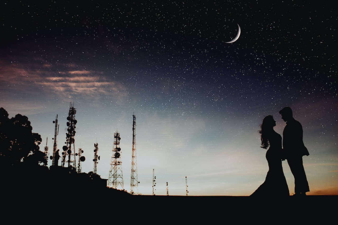 Silhouette of a Man and Woman Standing Outdoors With Satellites in the Background