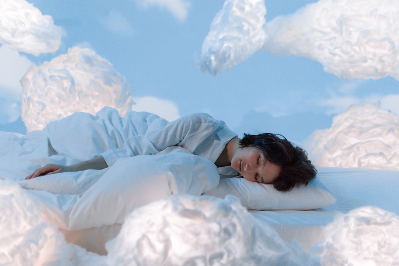 An adult woman in white sleepwear and in a dream state surrounded by fluffy white clouds