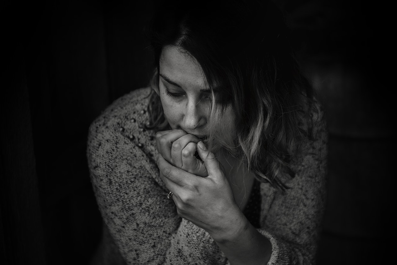 An adult woman in long-sleeved top and in an anxious state, sitting and biting her nails