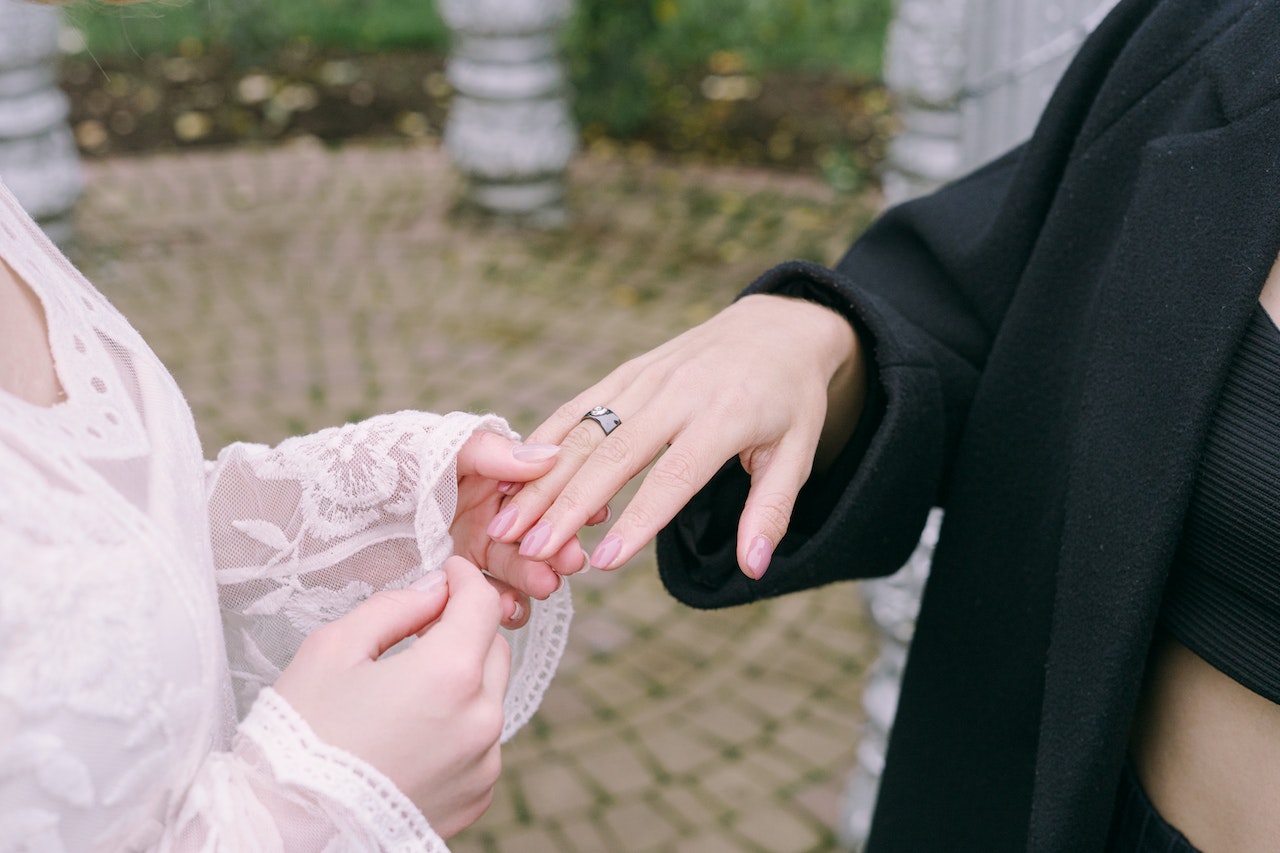 Hand of Woman in White Lace Dress Holding Hand of Woman in Black Coat
