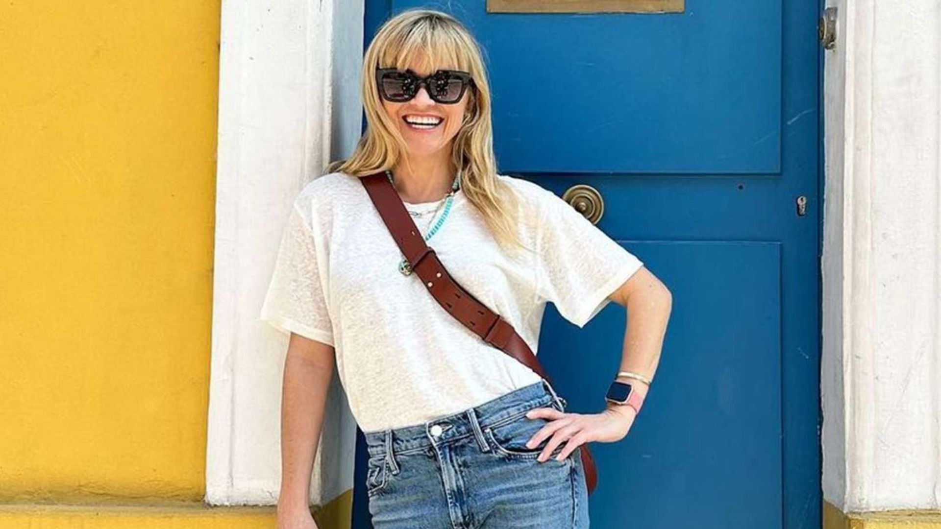 Reese Witherspoon Smiling Standing In Front Of A Blue Door