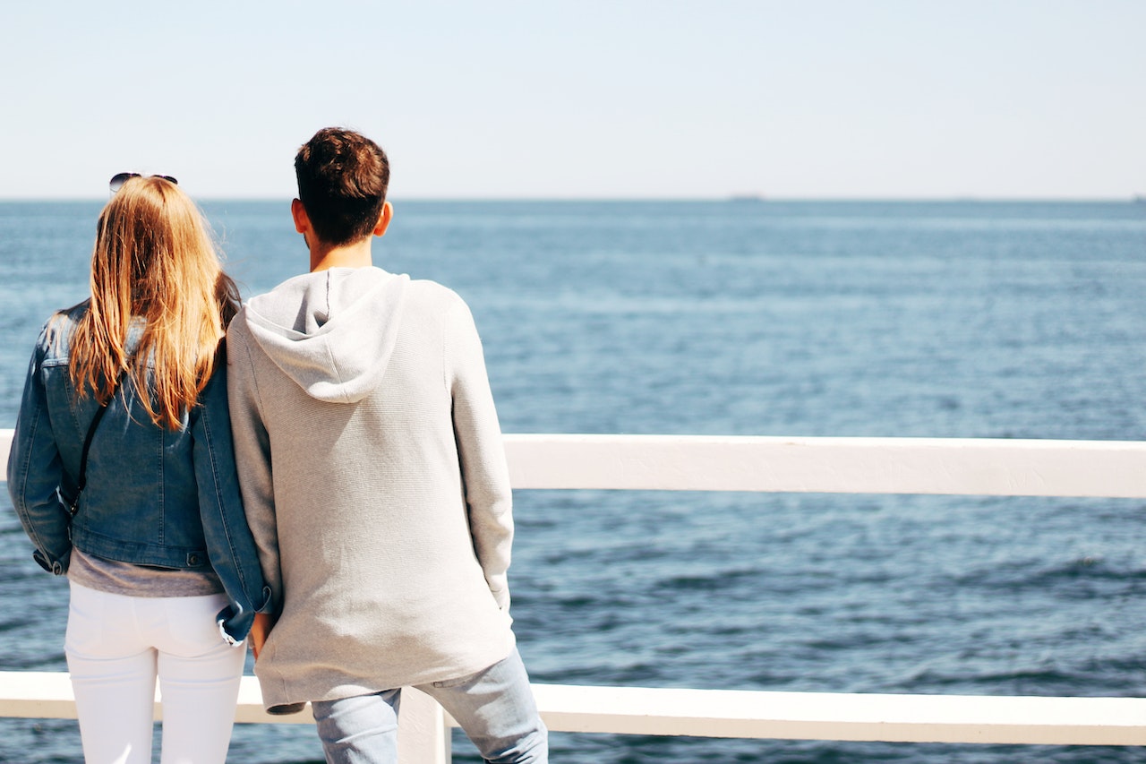 Man and Woman Beside a White Wooden Hand Rail Facing the Ocean