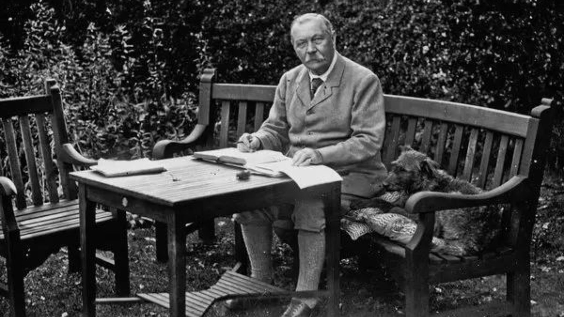 Sir Arthur Conan Doyle Sitting On A Wooden Bench With His Dog