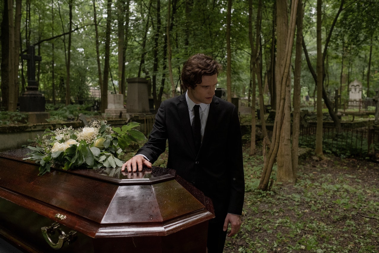 Man in Black Suit Standing near a Brown Coffin